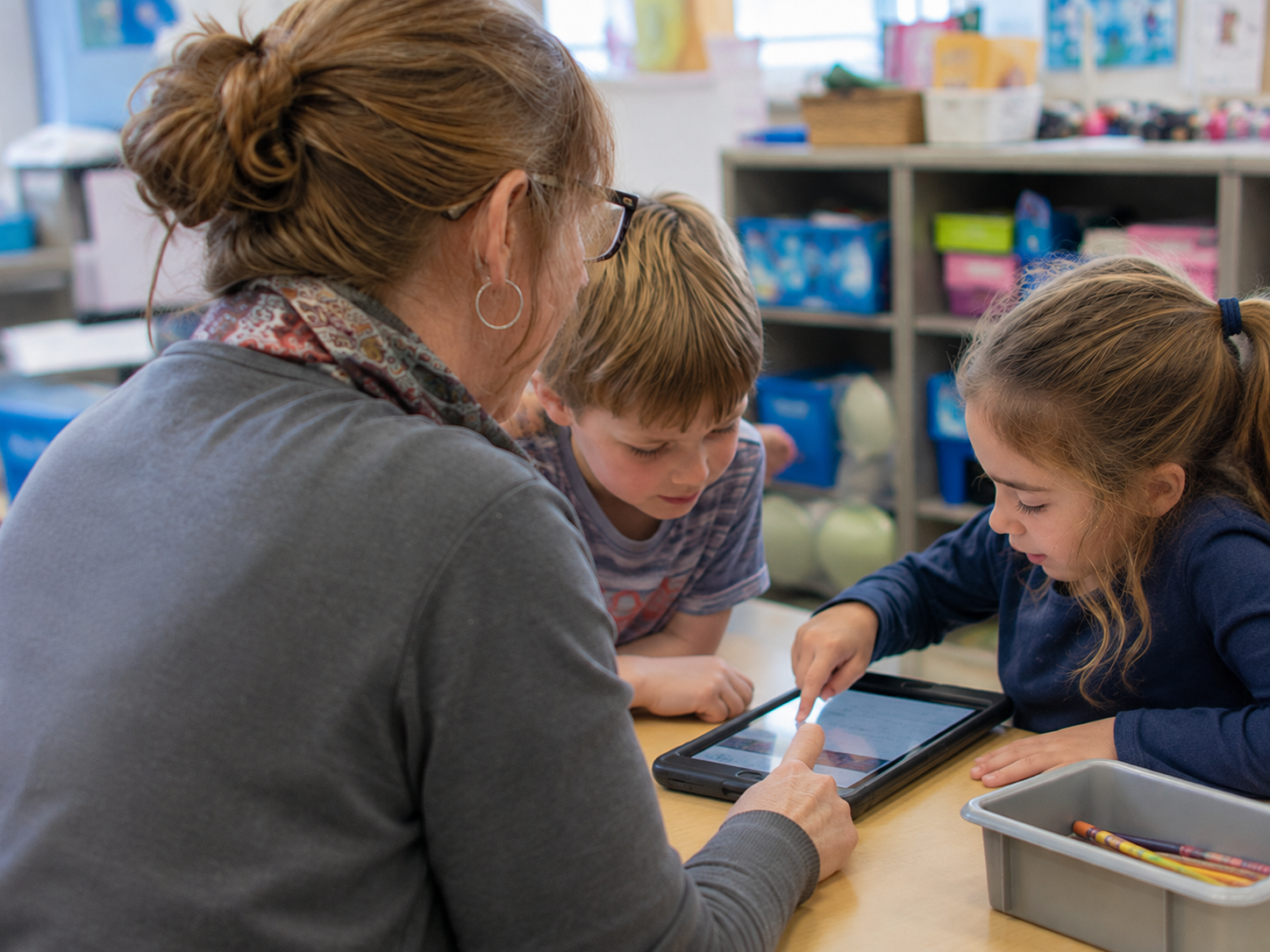 A teacher works closely with young students gathered around a classroom table