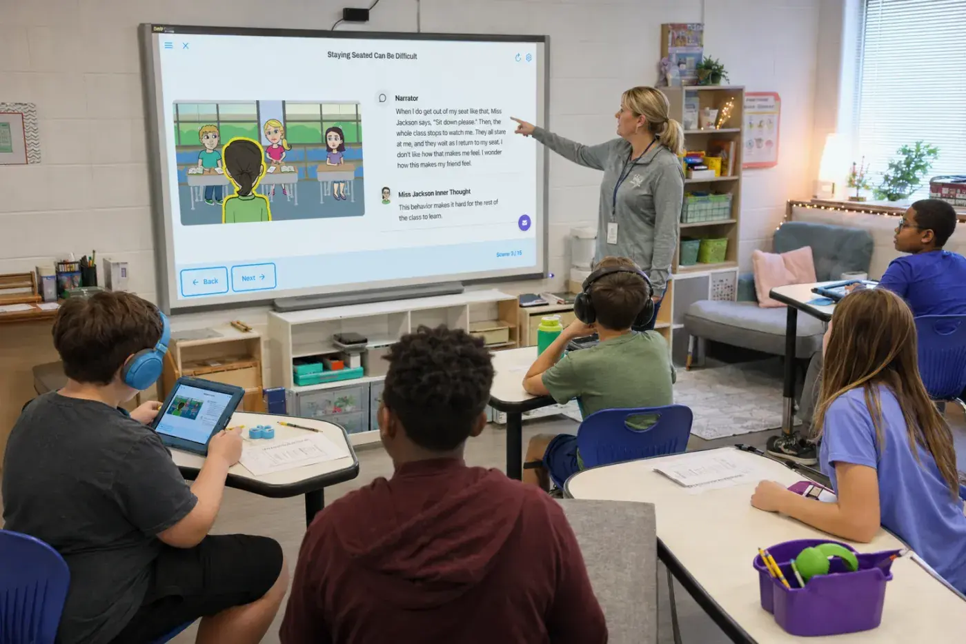 A teacher presents a Speech Kingdom social story on the classroom smartboard while students follow along on tablets